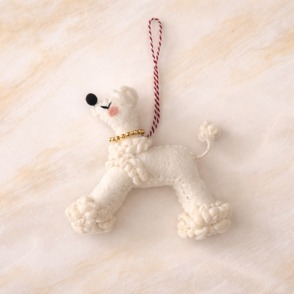 White poodle-shaped ornament with a gold collar on a soft beige background