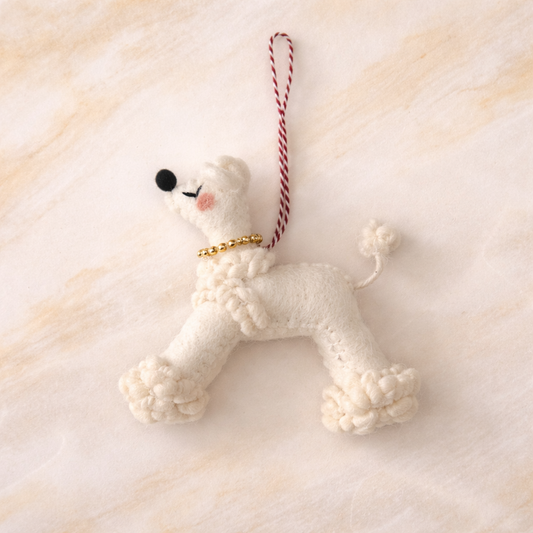 White poodle-shaped ornament with a gold collar on a soft beige background
