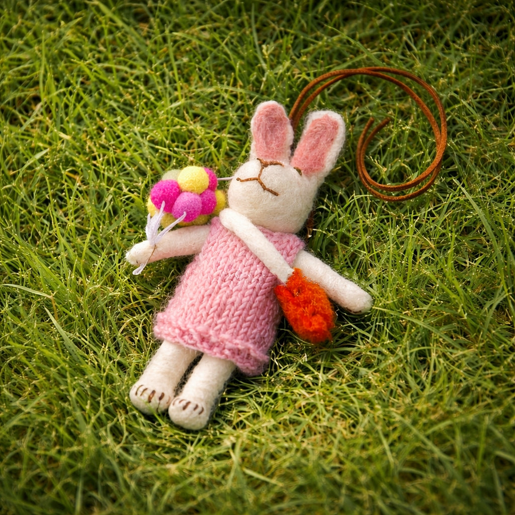 Knitted bunny toy in a pink dress lying on grass
